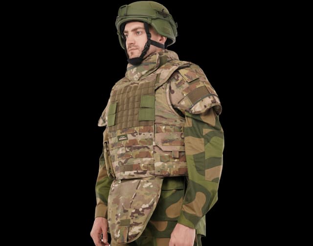 Man wearing Hard Shell camouflage Patron Vest with ballistic helmet, featuring neck, shoulder, and groin protection for military-grade safety.
